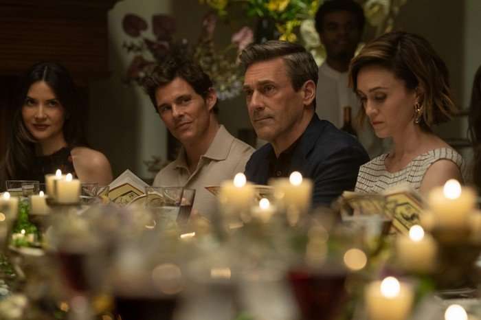 James Marsden and Jon Hamm sitting at an opulent dinner table with candles, surrounded by other people.
