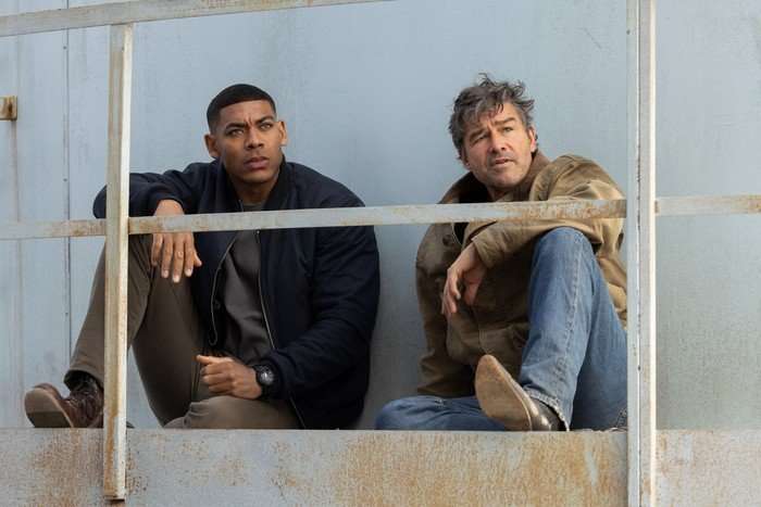 John Stewart and Hal Jordan sit on a metal structure with a rusted railing in front of them