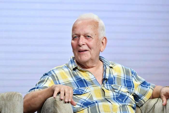 Andrew Davies, an older man with white hair, wearing a blue and yellow checked shirt, speaks on a panel while seated in an armchair.