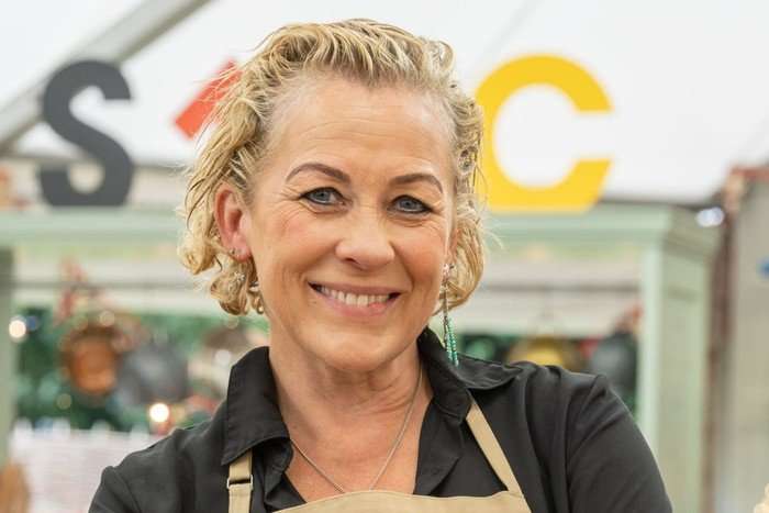 Sarah Beeny wearing a black shirt and brown apron, smiling ahead.