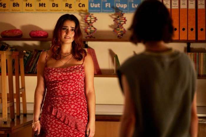 A Good Girl's Guide To Murder Naomi wearing a red dress, standing looking at Pip with tears in her eyes
