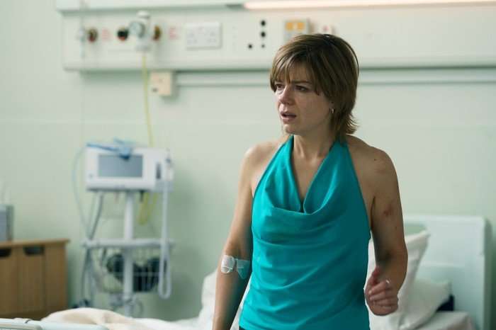 Aimee-Ffion Edwards as Sarah in Believe Me, sitting on the edge of a hospital bed, with a plaster on her arm, looking confused.