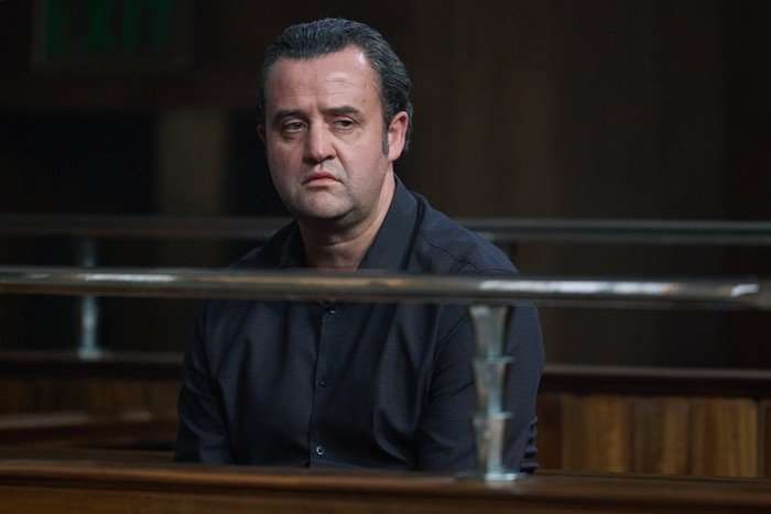BelieveMe_D42 Daniel Mays as John Worboys in Believe Me sitting in the court stand, wearing a shirt and looking forlorn as he stares across the room.
