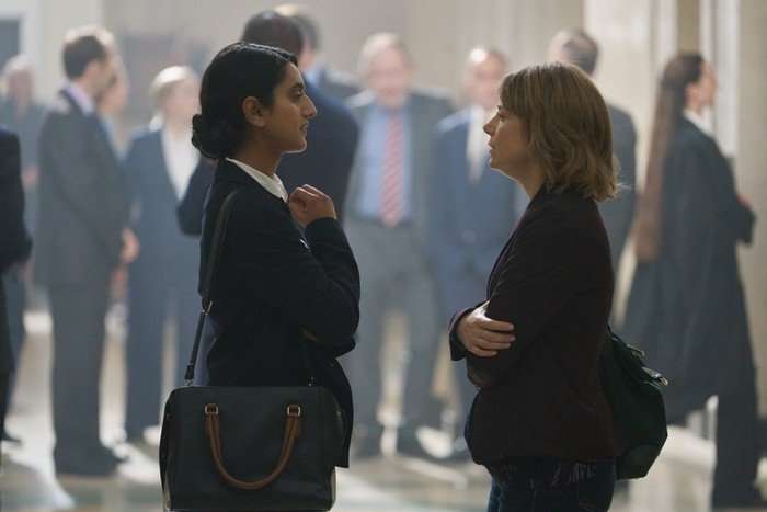 Aasiya Shah and Aim&eacute;e-Ffion Edwards standing in a crowded hallway in a courthouse, looking at each other as they have a conversation.
