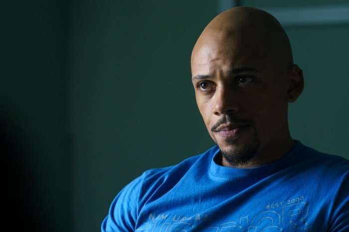 Jordan Bolger as Connor in Believe Me sitting in a waiting room, wearing a blue t-shirt and looking blankly at the other side of the room.
