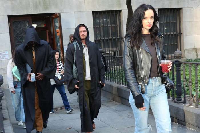 Mike Colter, Finn Jones and Krysten Ritter walk side by side in costume on a Brooklyn street set during Daredevil: Born Again season 3 filming, surrounded by crew and production equipment in April 2026