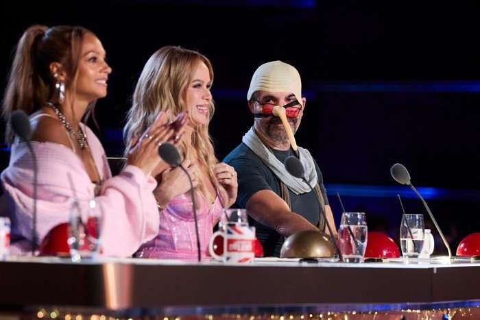Alesha Dixon, Amanda Holden and Simon Cowell on Britain's Got Talent Simon Cowell wearing a bizarre bald cap and long thin nose, with red-tinted glasses on, sitting on the BGT panel alongside Alesha Dixon and Amanda Holden, who are smiling at what they're watching.