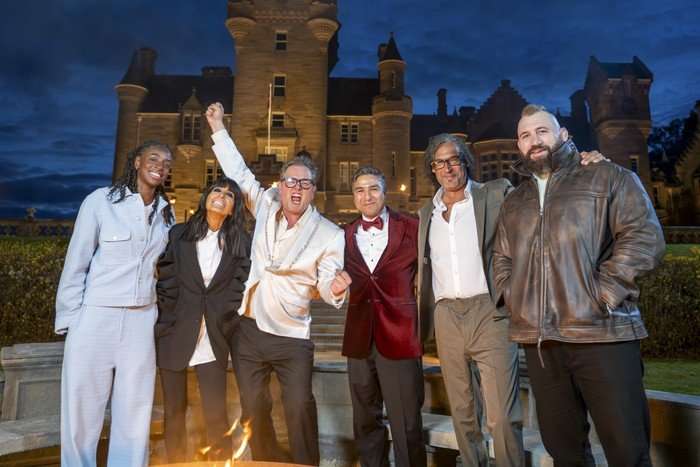 Cat Burns, Claudia Winkleman, Alan Carr, Nick Mohammed, David Olusoga & Joe Marler stood next to each other smiling ahead as Alan Carr raising one hand in the air.
