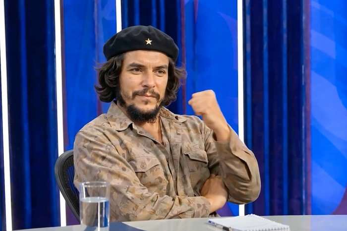 AI-generated depiction of Che Guevara seated on the Question Time set, wearing a black beret and khaki shirt while raising one fist against a blue studio backdrop.