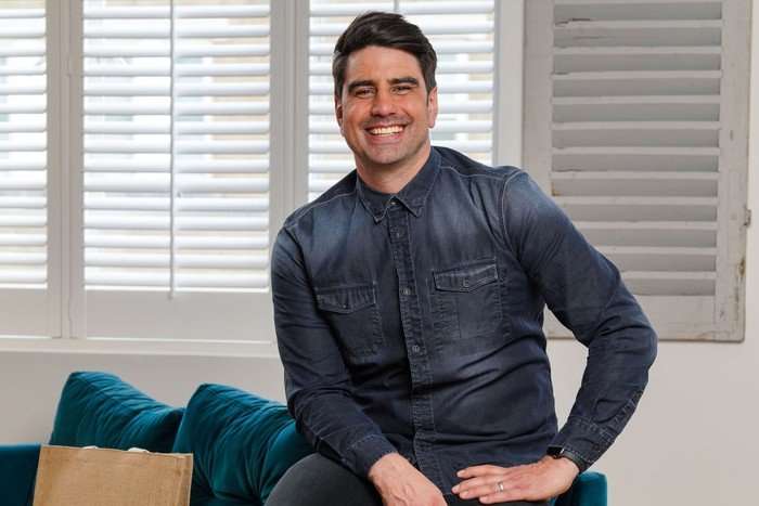 Chris Bavin sat down on a chair wearing a charcoal shirt.