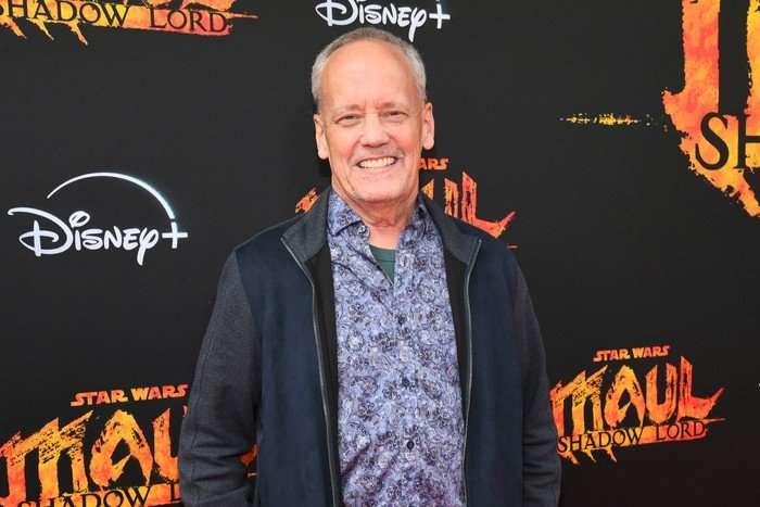 Dee Bradley Baker photographed at the Maul: Shadow Lord premiere. He is wearing a shirt and jacket and smiling enthusiastically for the camera.