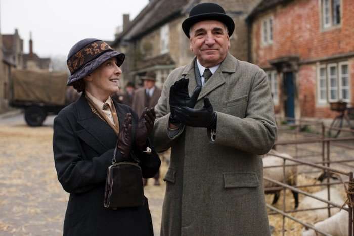Phyllis Logan as Mrs Hughes and Jim Carter as Mr Carson in Downton Abbey. They are outdoors wearing coats, gloves and hats. Mr Carter is clapping his hands together and Mrs Hughes is looking up at him, and both are happy.
