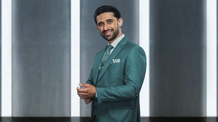 Omar stood with his body turned to one side, wearing a blue suit.