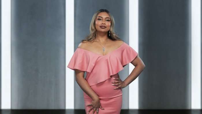 Parissa wearing a pink dress, posing with one hand placed on her hip.