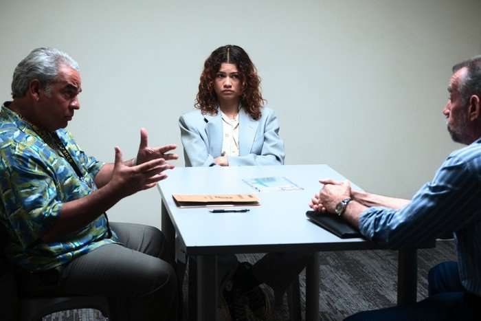 Hemky Madera, Zendaya, Bill Bodner in Euphoria season 3 sitting in a police station interview room, looking uneasy.