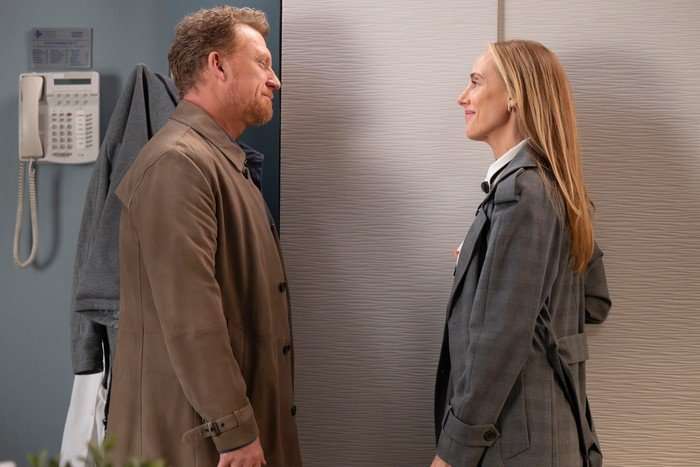 Kevin McKidd and Kim Raver in Grey's Anatomy season 22 standing in front of a lift together, facing each other and smiling.