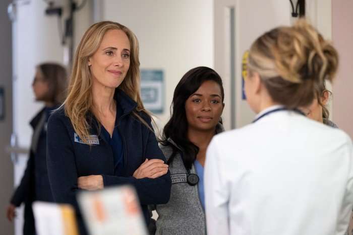 Kim Raver as Teddy in Grey's Anatomy standing in a hallway, smiling at a doctor while crossing her arms.