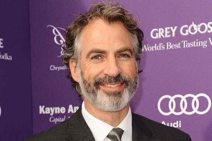 harry-van-gorkum Harry Van Gorkum smiles in a black suit and grey tie at a purple event red carpet.