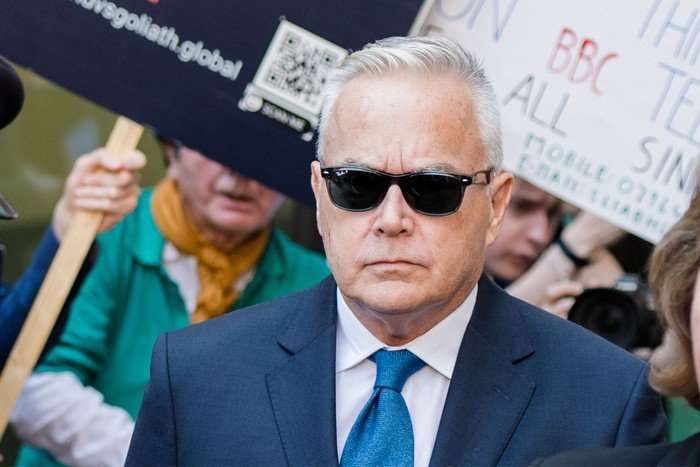 huw-edwards Huw Edwards wearing a blue suit and tie, with black sunglasses on looking ahead with a mute expression.