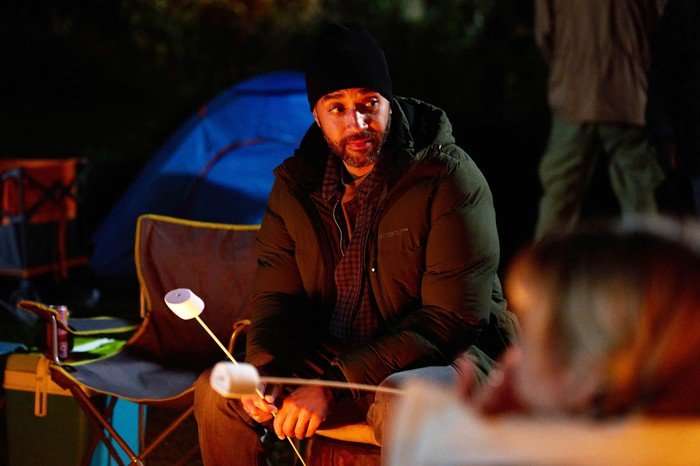 Samuel Anderson plays Mal, sat around a campfire roasting a marshmallow