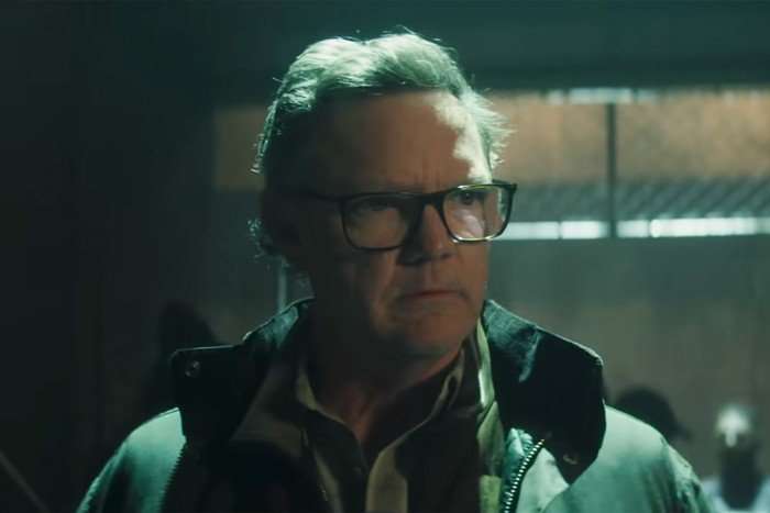 Mr Charles wears a coat and glasses as he surveys a warehouse in a scene from Daredevil: Born Again