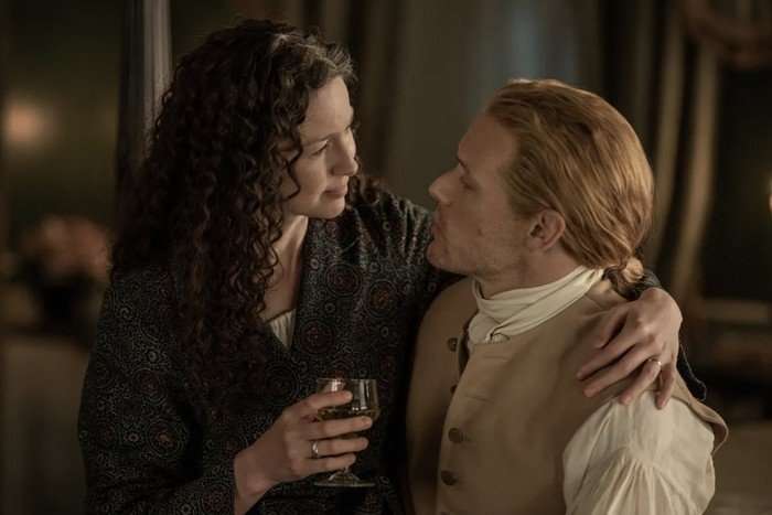 Caitr&iacute;ona Balfe and Sam Heughan in an embrace and looking into each other's eyes.