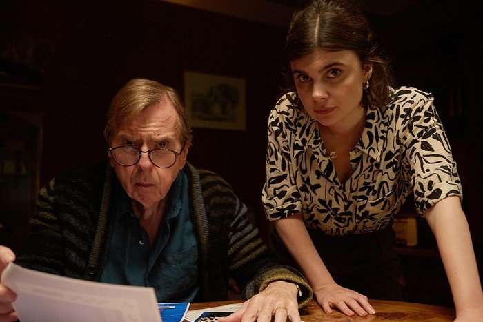 Timothy Spall as John Chapel and Gwyneth Keyworth as Janie Mallowan in Death Valley. He is sat at a desk, she is stood next to him, and they are both looking into the camera