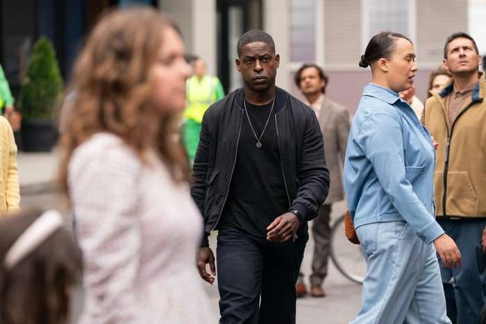 Sterling K Brown looking stern and wearing an all black outfit as he walks through a crowd of people.