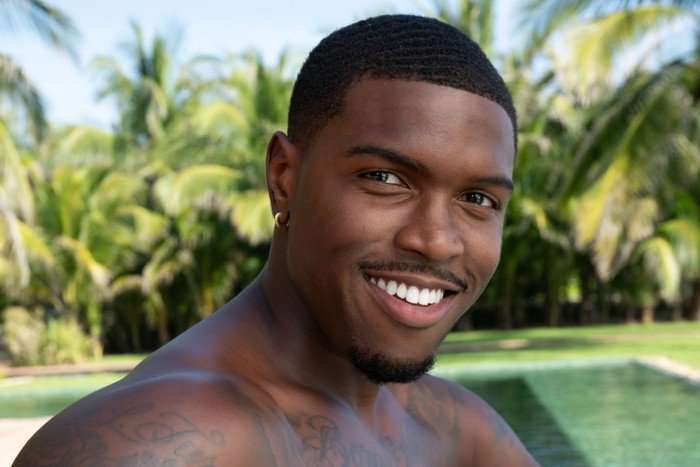 A man sat in front of a swimming pool smiling ahead.