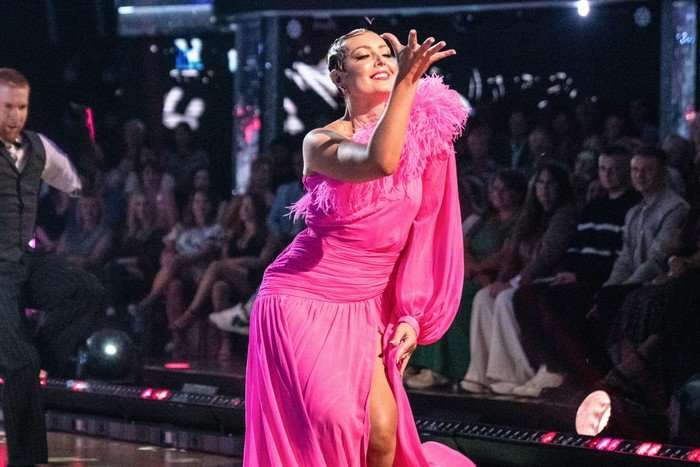 Amy Dowden wearing a pink ball gown, smiling as she performs.