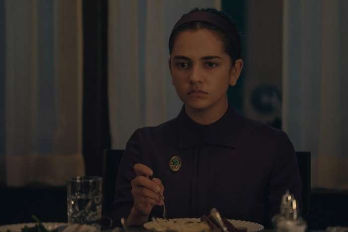 MATTEA CONFORTI Mattea Conforti in The Testaments, sitting at her dinner table with her fork poised and looking sternly and blankly in the distance.