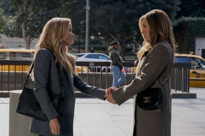the-morning-show-season-3-reese-witherspoon-jennifer-aniston Reese Witherspoon and Jennifer Aniston as Bradley and Alex in The Morning Show, holding hands on a pavement.