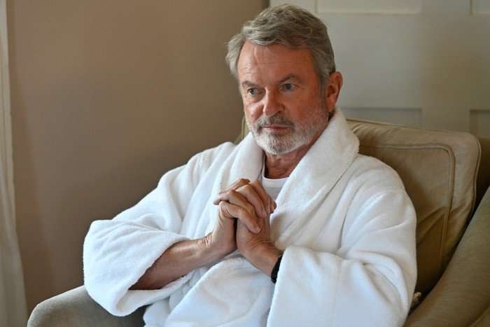 The Twelve Season 2 Sam Neill as Brett Colby in The Twelve Season 2, wearing a bathrobe and sat in a chair