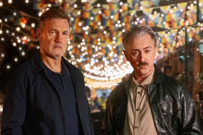 Clive and Leo from Tip Toe, standing on Canal Street, decorated with fairy lights and Pride flags, looking annoyed at each other