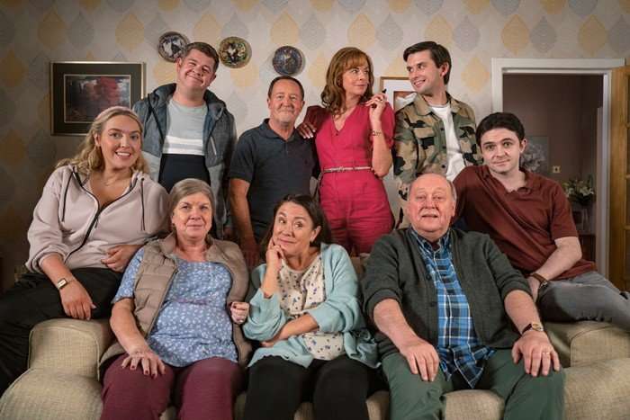 The cast of Two Doors Down season 7 gathered around a sofa posing for the camera