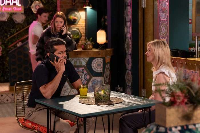 05_07_coro_idris_abi_01 Abi on the phone in the background, as Idris, who is sat opposite Leanne, takes a call in the foreground of a scene in Coronation Street