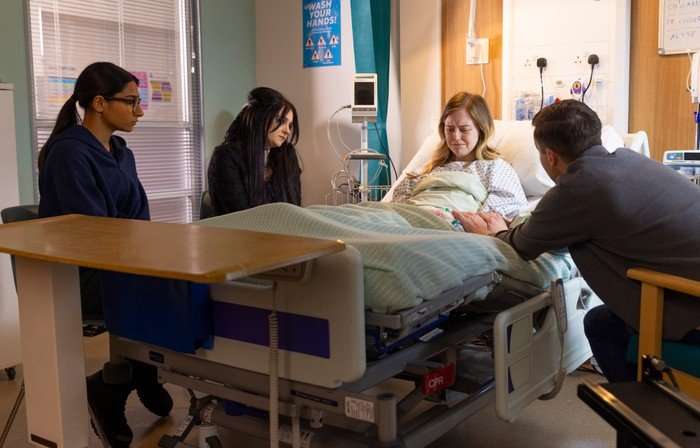 Asha, Nina and Todd gather around Summer's hospital bed in a scene from Coronation Street