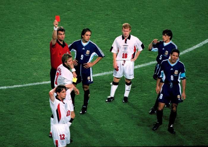 Fifa World Cup 1998 Footballers standing on a pitch staring intently as a referee holds up a red card.