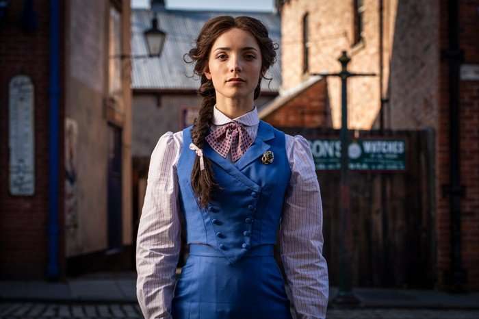 Jessica Reynolds in A Woman of Substance Jessica Reynolds as Emma Harte in A Woman of Substance, wearing a blue waistcoat, shirt and tie as she stands in the middle of a road.