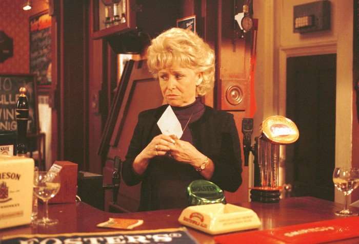Barbara Windsor as Pegg yMitchell stands holding a letter behind the Queen Vic pub bar in EastEnders.