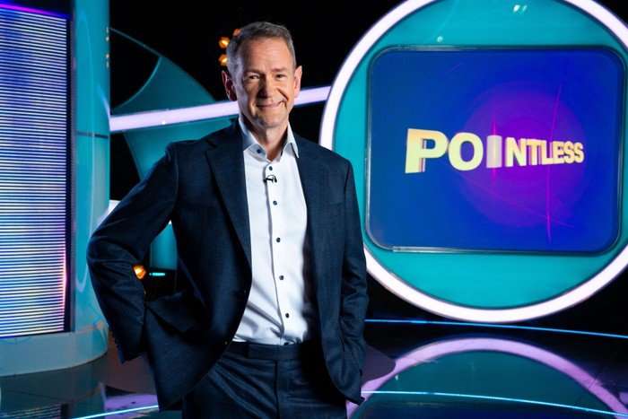 523795,TITLE:Pointless S34 Alexander Armstrong stood next to the Pointless screen, smiling ahead wearing a light blue shirt and a dark blue suit.