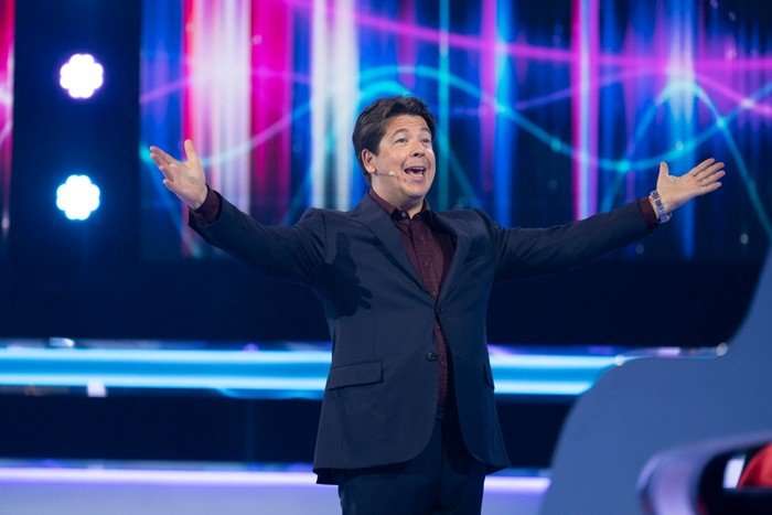 534948,TITLE:Michael McIntyre's The Wheel S6 Michael McIntyre wearing a dark blue sit with his arms stretched out in celebration.
