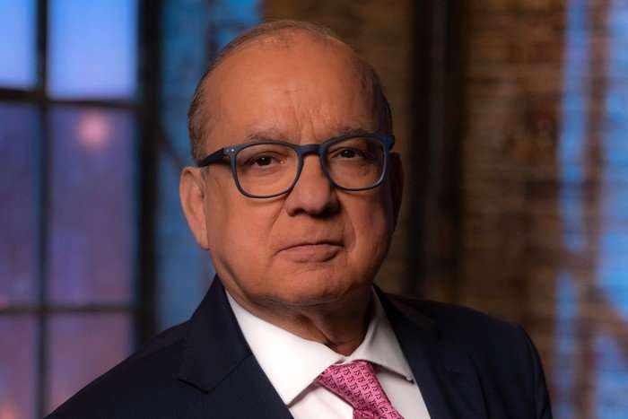 Touker Suleyman. for Dragon's Den, wearing a blue suit, white shirt and pink tie.