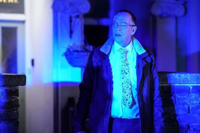 Ian steps out of his house in a flood of blue lights from a police car in a scene from EastEnders