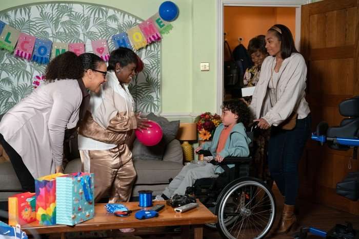 564816,TITLE:Eastenders Kim and Libby stand over Jordan, who is being wheeled into a living room by Chelsea in a scene from EastEnders