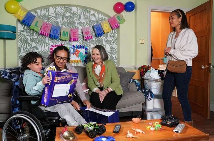 564829,TITLE:Eastenders Chelsea stands over Sheila, Libby and Jordan, who is opening a toy, in a scene from EastEnders