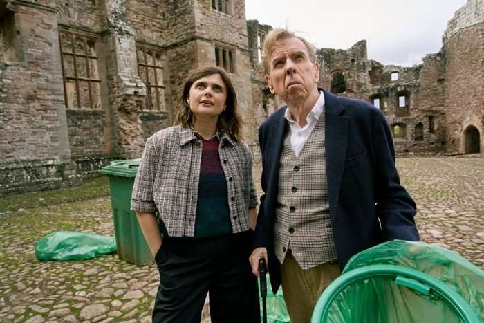 DCI Janie Mallowan and John Chapel stood outside a historic building, surrounded by light green bins, looking up into the distance