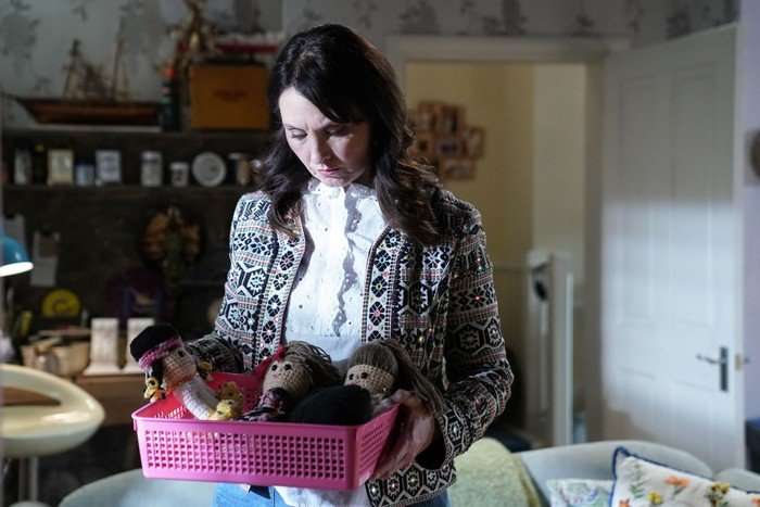 566258,TITLE:Eastenders Honey stands in her living room over a box of crocheted dolls in a scene from EastEnders
