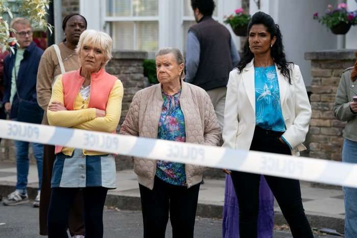 Jean, Mo and Suki stand behind a police cordon in EastEnders