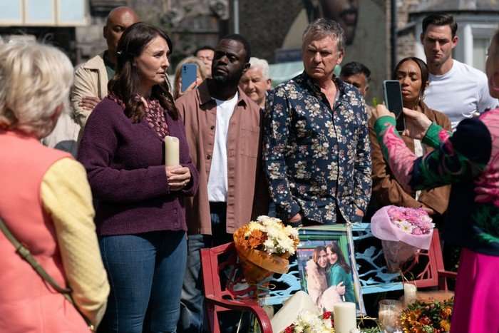 Linda films a vigil for Honey, where she stands over a bench with some flowers and a picture of her and Bea in a scene from EastEnders